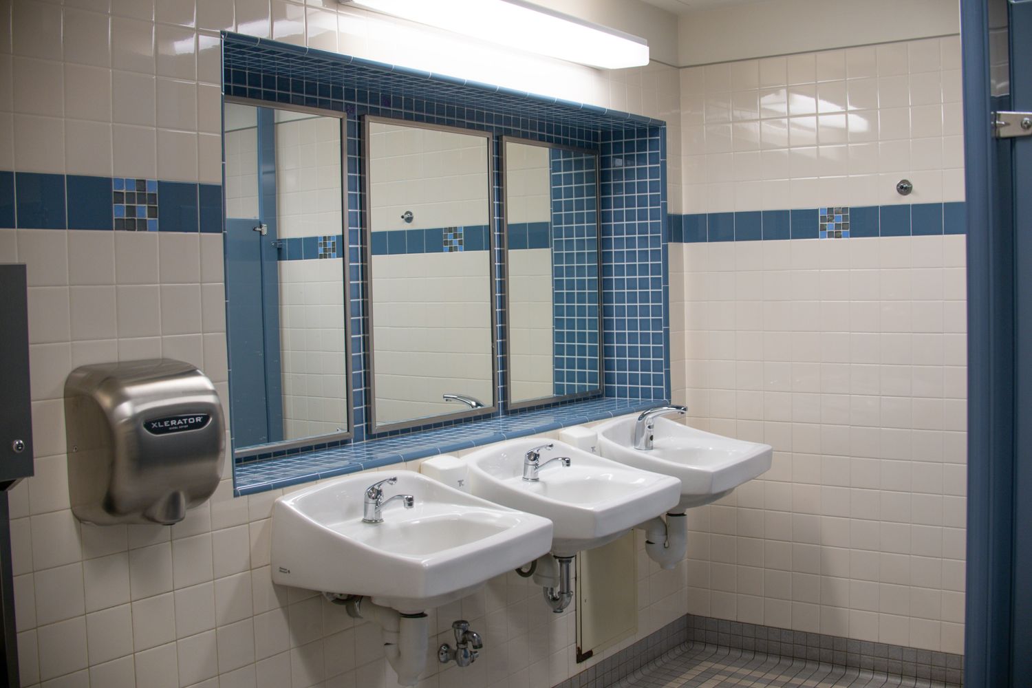 Clean commercial restroom with sinks, mirrors, tile, and a hand dryer